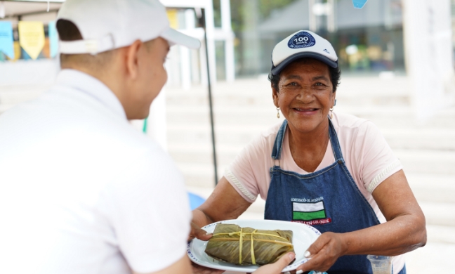 Mujer adulta sonriendo mientras entrega a un hombre un plato con comida tradicional
